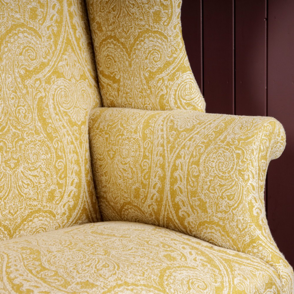 A high-backed Regency wingback armchair upholstered in patterned yellow fabric with turned mahogany front legs on brass castors. View III