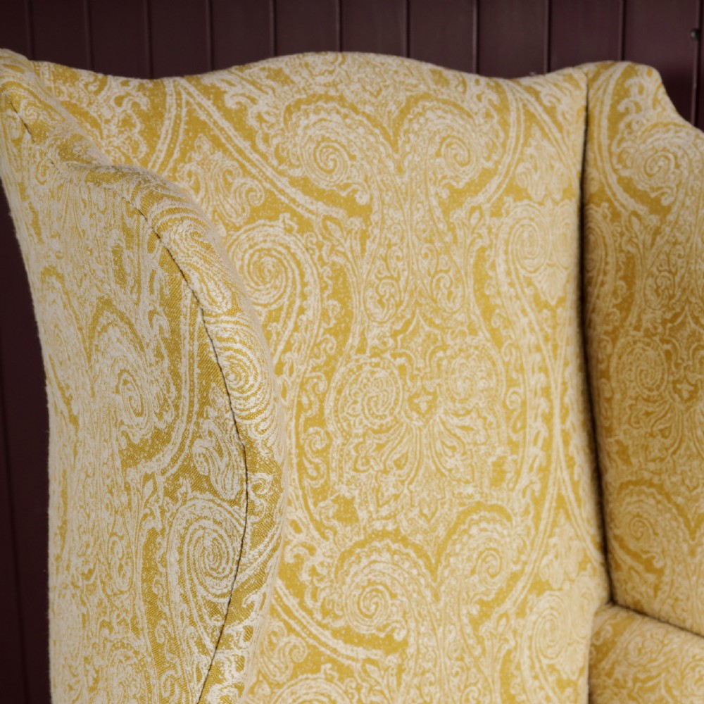 A high-backed Regency wingback armchair upholstered in patterned yellow fabric with turned mahogany front legs on brass castors. View IV