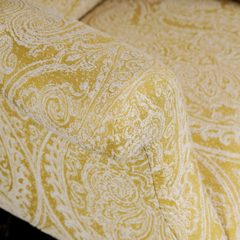 A high-backed Regency wingback armchair upholstered in patterned yellow fabric with turned mahogany front legs on brass castors. View V