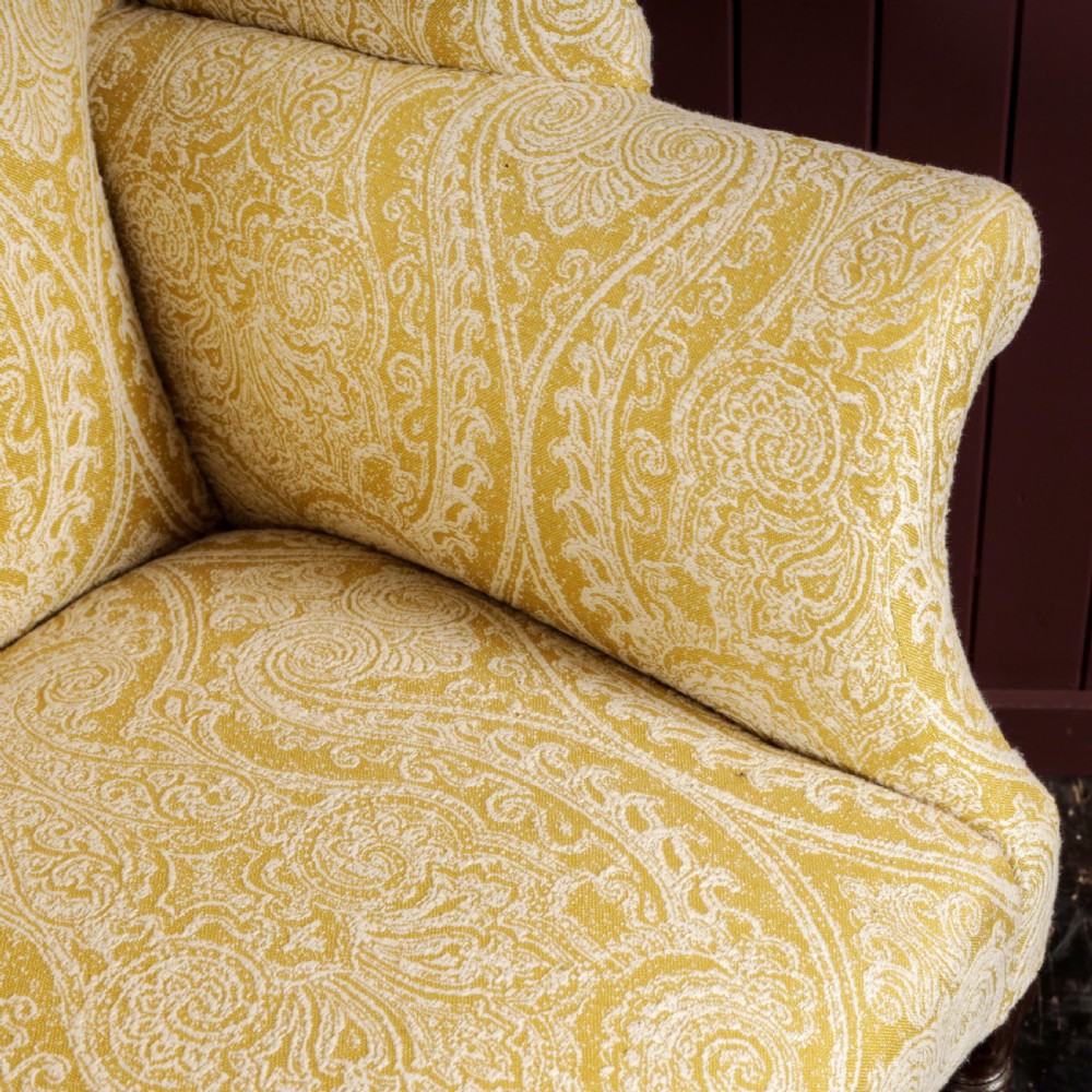 A high-backed Regency wingback armchair upholstered in patterned yellow fabric with turned mahogany front legs on brass castors. View VI