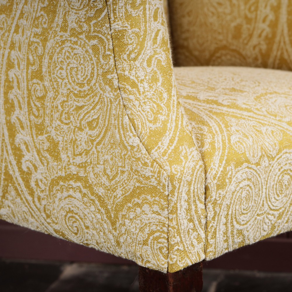 A high-backed Regency wingback armchair upholstered in patterned yellow fabric with turned mahogany front legs on brass castors. View VII