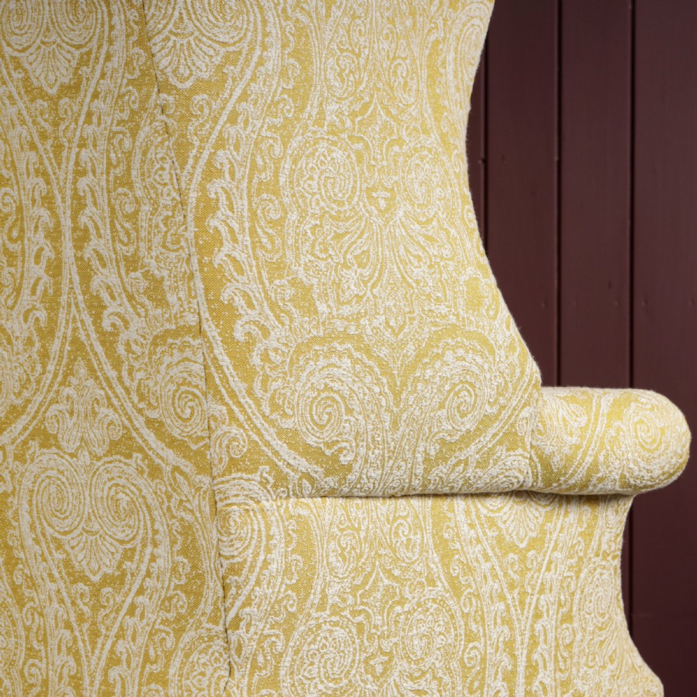A high-backed Regency wingback armchair upholstered in patterned yellow fabric with turned mahogany front legs on brass castors. View VIII