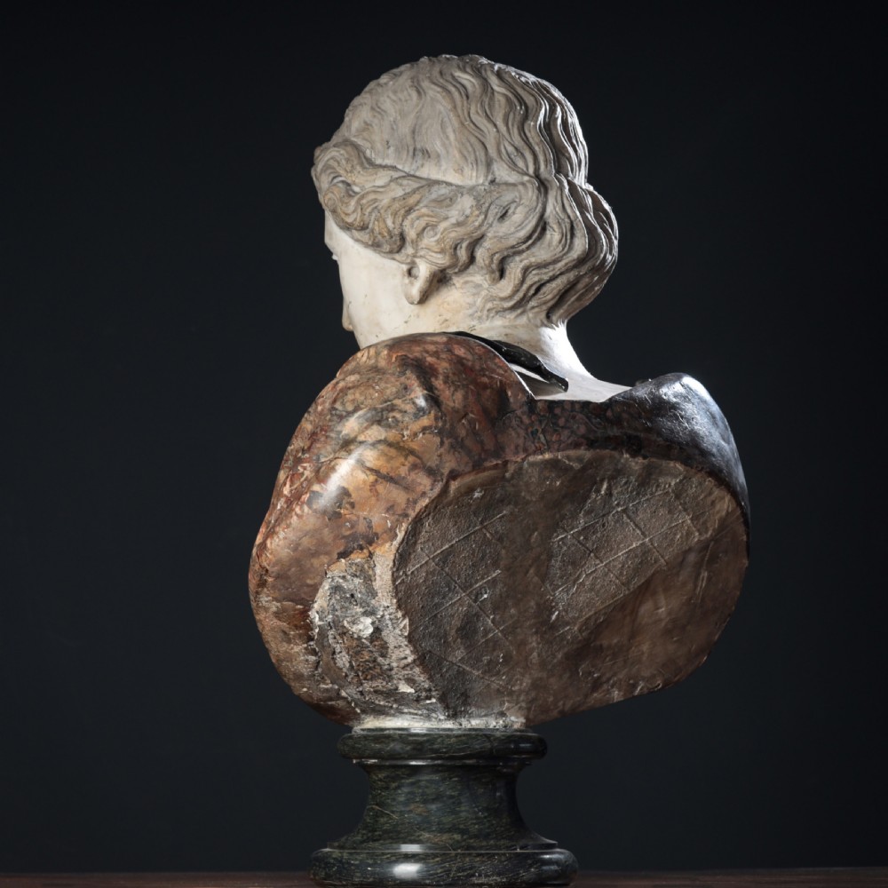 A carved marble profile bust depicting a woman with wavy hair gathered in a bun, wearing dark draped robes, set upon a turned marble socle. View XIV
