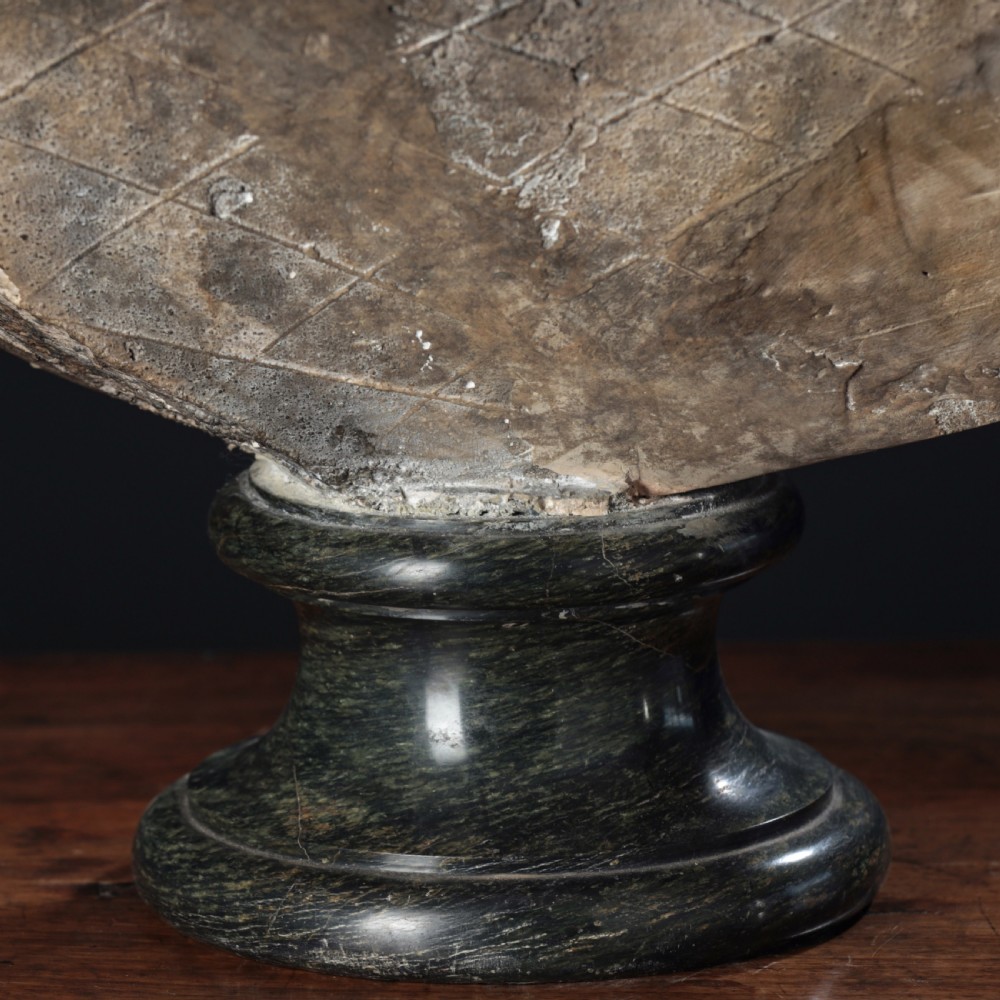 A carved marble profile bust depicting a woman with wavy hair gathered in a bun, wearing dark draped robes, set upon a turned marble socle. View XVI