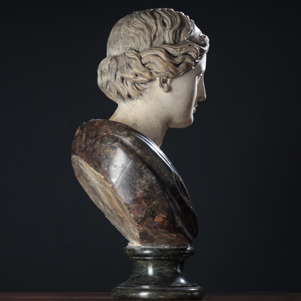 A carved marble profile bust depicting a woman with wavy hair gathered in a bun, wearing dark draped robes, set upon a turned marble socle. View XXII