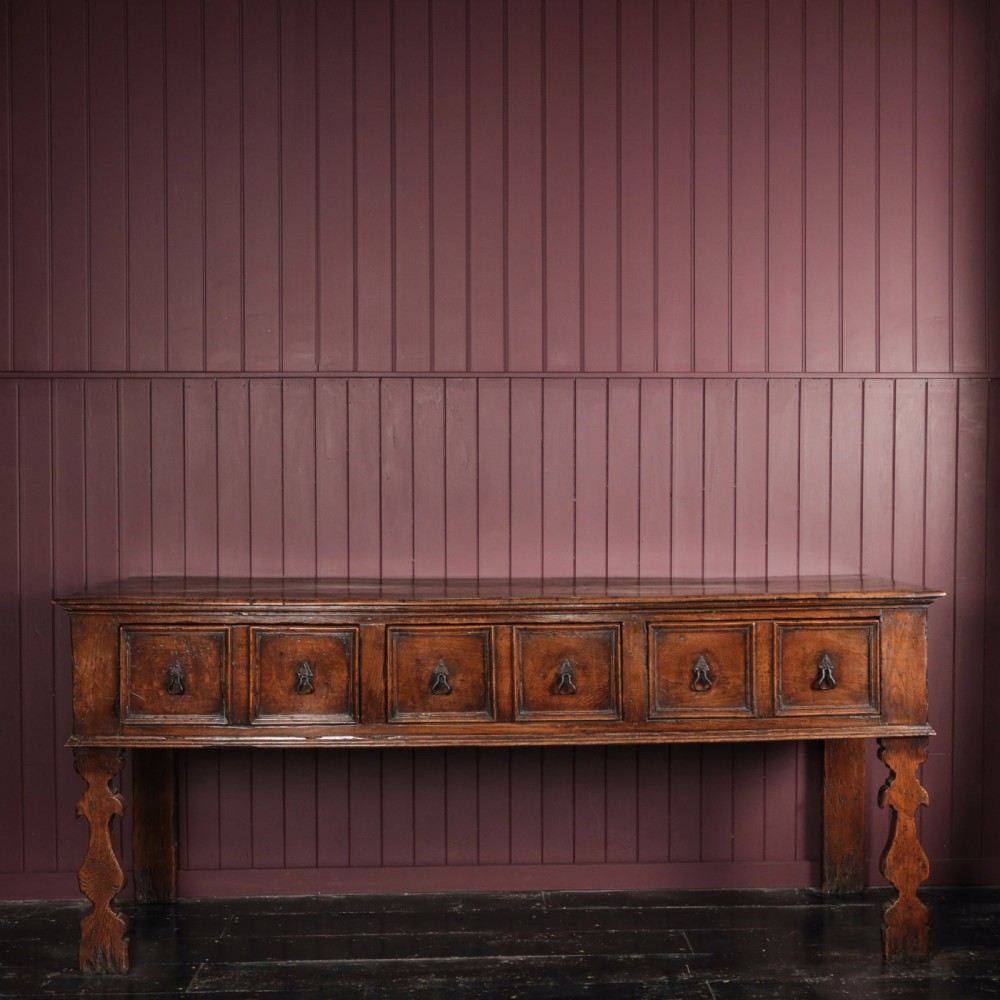 A long 17th-century dark oak dresser base featuring six geometric-moulded drawer fronts with iron teardrop handles and shaped legs.