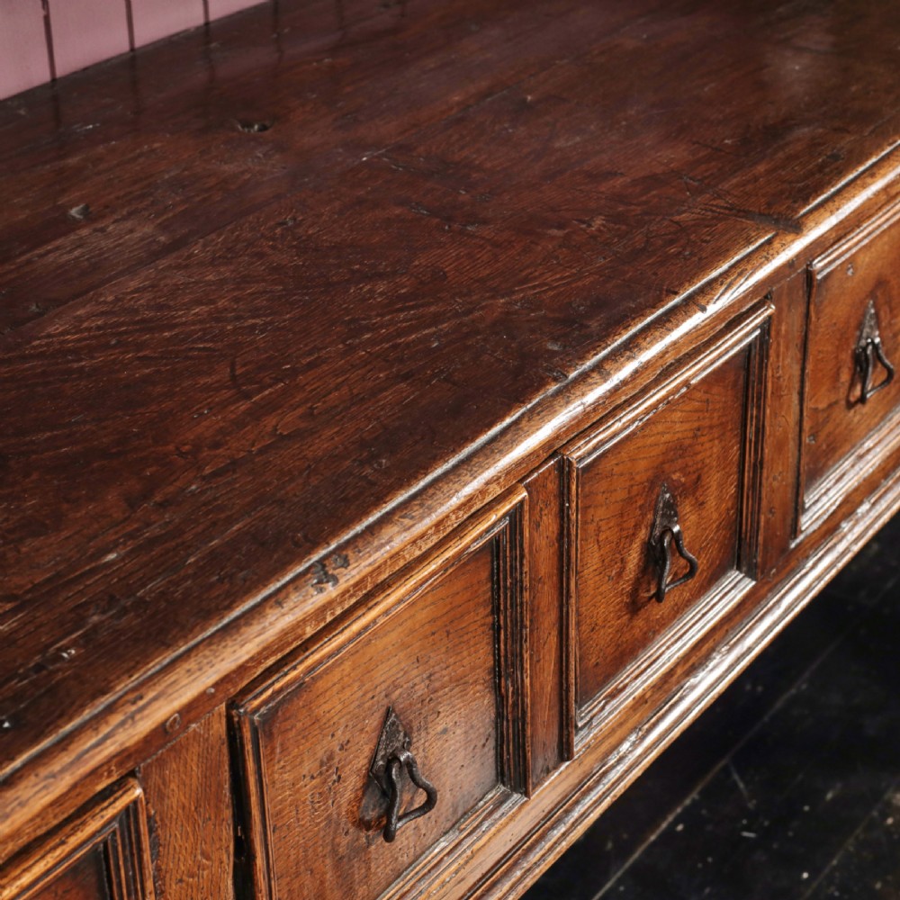 A long 17th-century dark oak dresser base featuring six geometric-moulded drawer fronts with iron teardrop handles and shaped legs. View II