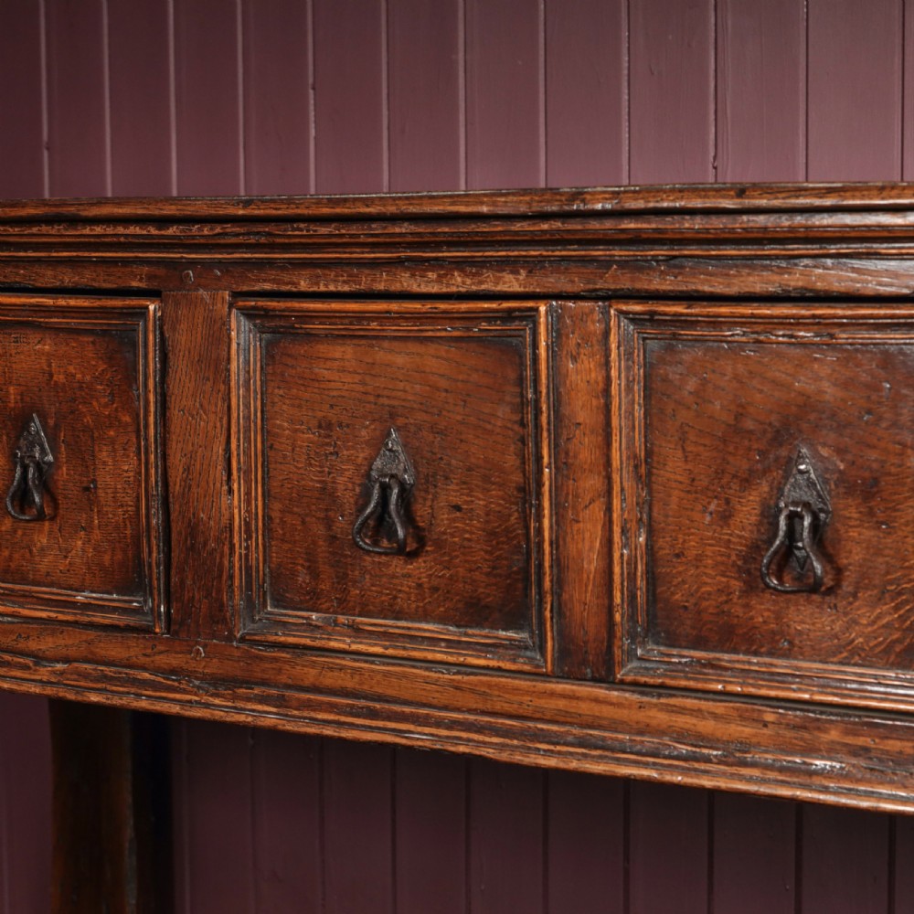 A long 17th-century dark oak dresser base featuring six geometric-moulded drawer fronts with iron teardrop handles and shaped legs. View III