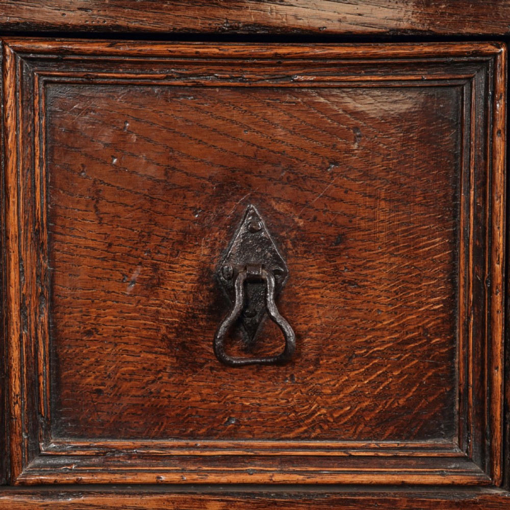 A long 17th-century dark oak dresser base featuring six geometric-moulded drawer fronts with iron teardrop handles and shaped legs. View VII