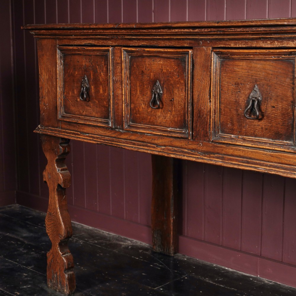 A long 17th-century dark oak dresser base featuring six geometric-moulded drawer fronts with iron teardrop handles and shaped legs. View VIII