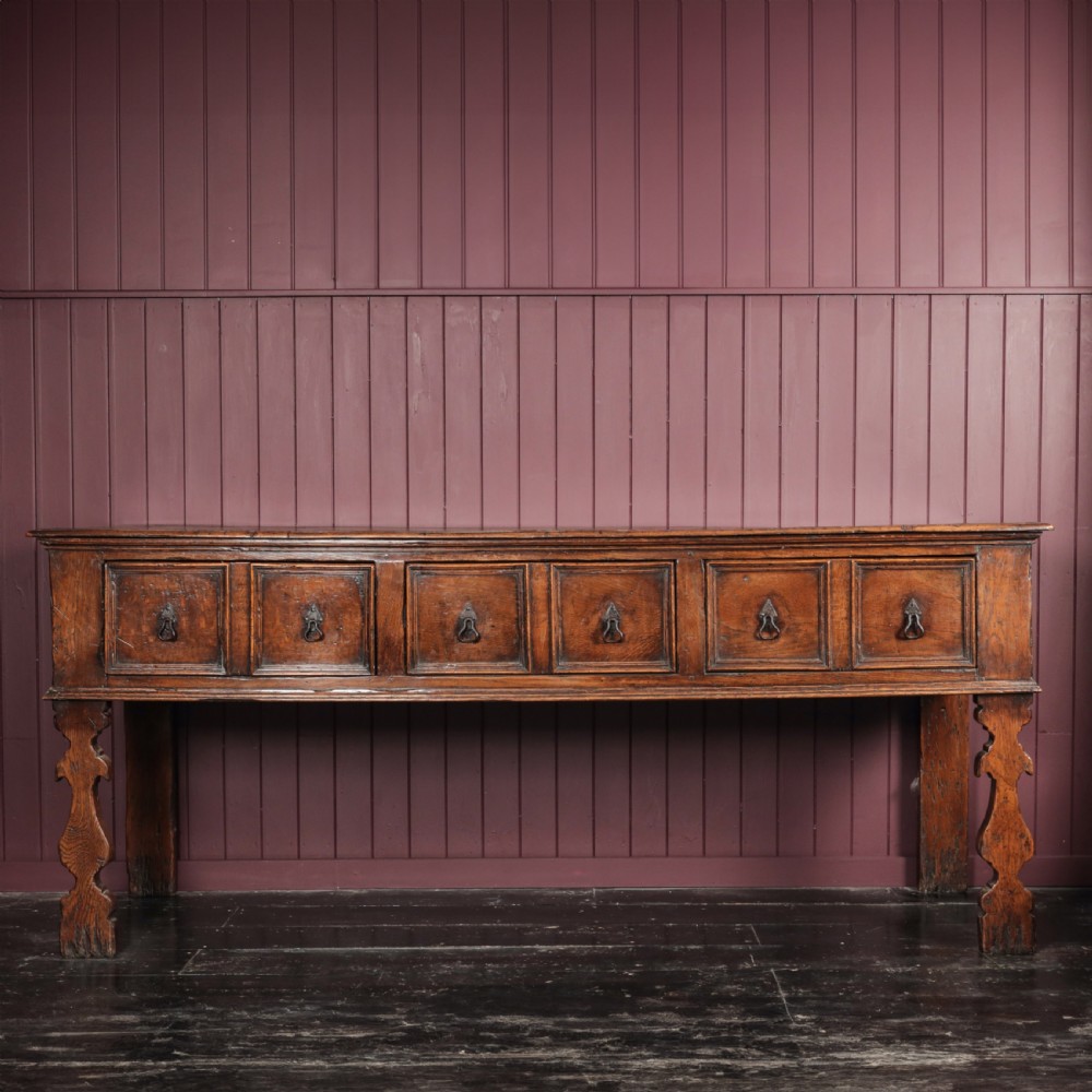 A long 17th-century dark oak dresser base featuring six geometric-moulded drawer fronts with iron teardrop handles and shaped legs. View XI