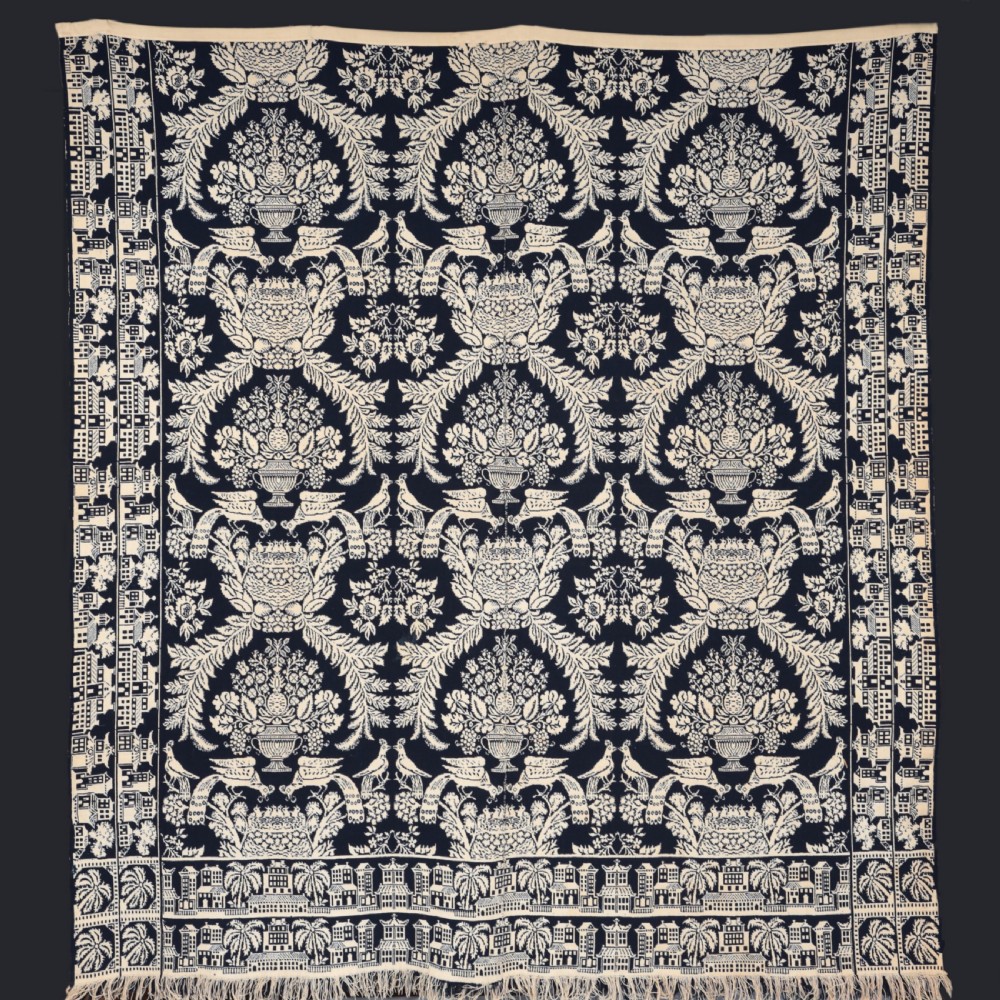 A nineteenth-century woven Jacquard coverlet in navy blue and cream featuring repeating floral urns, birds, and an architectural border with fringe. View II