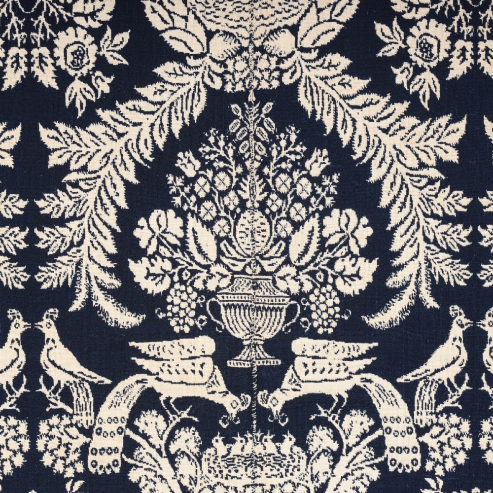 A nineteenth-century woven Jacquard coverlet in navy blue and cream featuring repeating floral urns, birds, and an architectural border with fringe. View VII