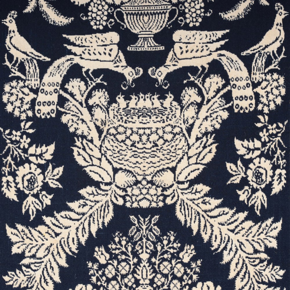 A nineteenth-century woven Jacquard coverlet in navy blue and cream featuring repeating floral urns, birds, and an architectural border with fringe. View IX