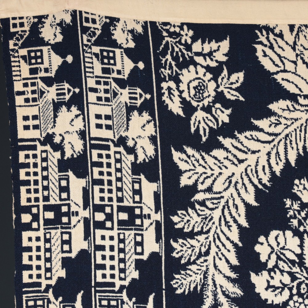A nineteenth-century woven Jacquard coverlet in navy blue and cream featuring repeating floral urns, birds, and an architectural border with fringe. View XIV