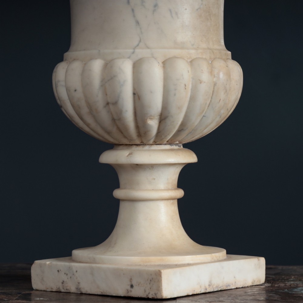 A pair of hand-carved white marble campana urns featuring gadrooned lower bodies and flared rims raised on square plinths. View IV