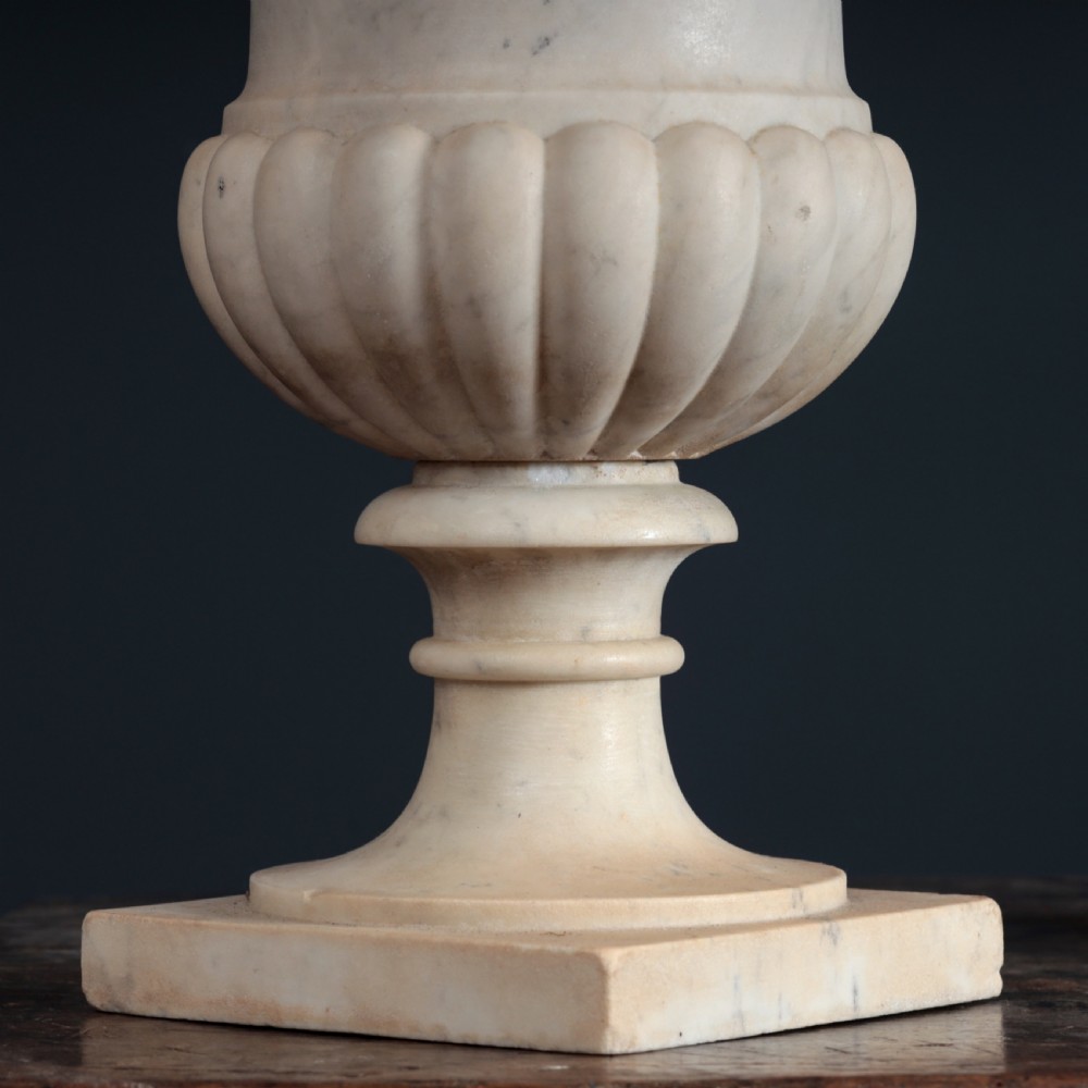 A pair of hand-carved white marble campana urns featuring gadrooned lower bodies and flared rims raised on square plinths. View VII