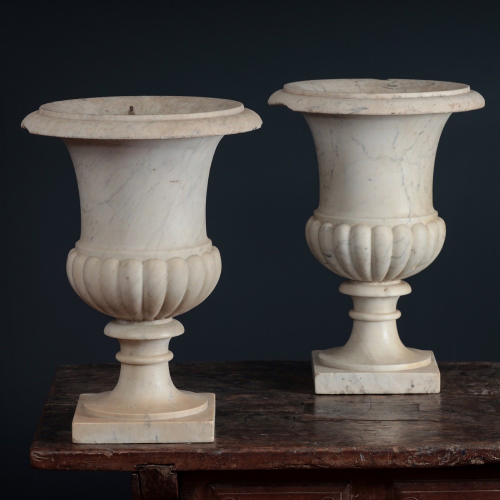 A pair of hand-carved white marble campana urns featuring gadrooned lower bodies and flared rims raised on square plinths. View VIII