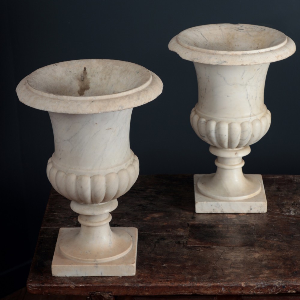 A pair of hand-carved white marble campana urns featuring gadrooned lower bodies and flared rims raised on square plinths. View IX