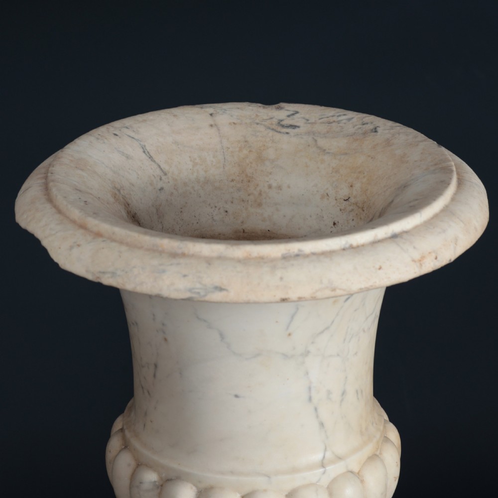 A pair of hand-carved white marble campana urns featuring gadrooned lower bodies and flared rims raised on square plinths. View X