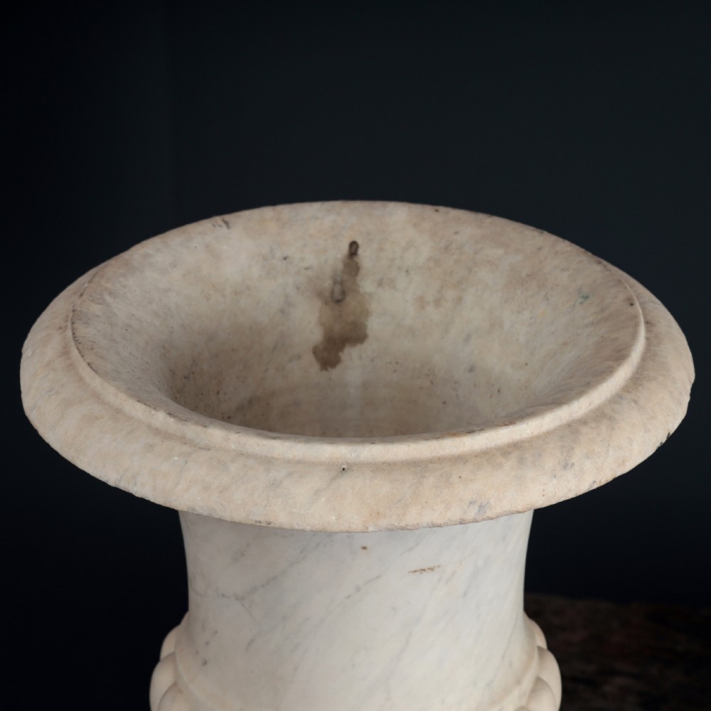 A pair of hand-carved white marble campana urns featuring gadrooned lower bodies and flared rims raised on square plinths. View XI