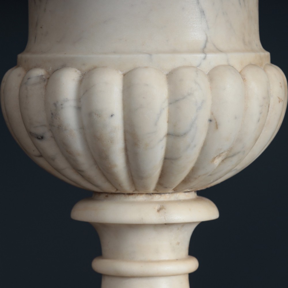 A pair of hand-carved white marble campana urns featuring gadrooned lower bodies and flared rims raised on square plinths. View XII