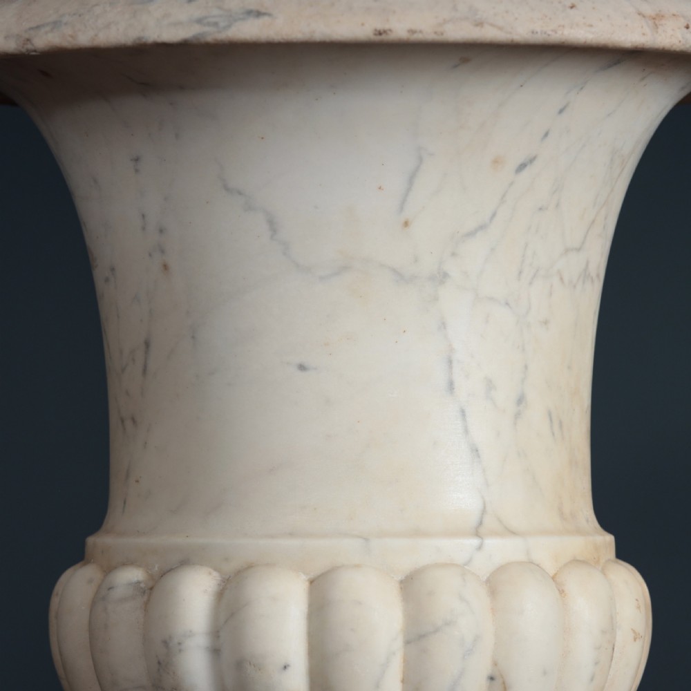A pair of hand-carved white marble campana urns featuring gadrooned lower bodies and flared rims raised on square plinths. View XIII