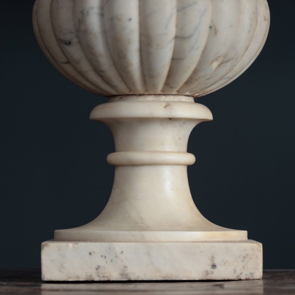 A pair of hand-carved white marble campana urns featuring gadrooned lower bodies and flared rims raised on square plinths. View XIV