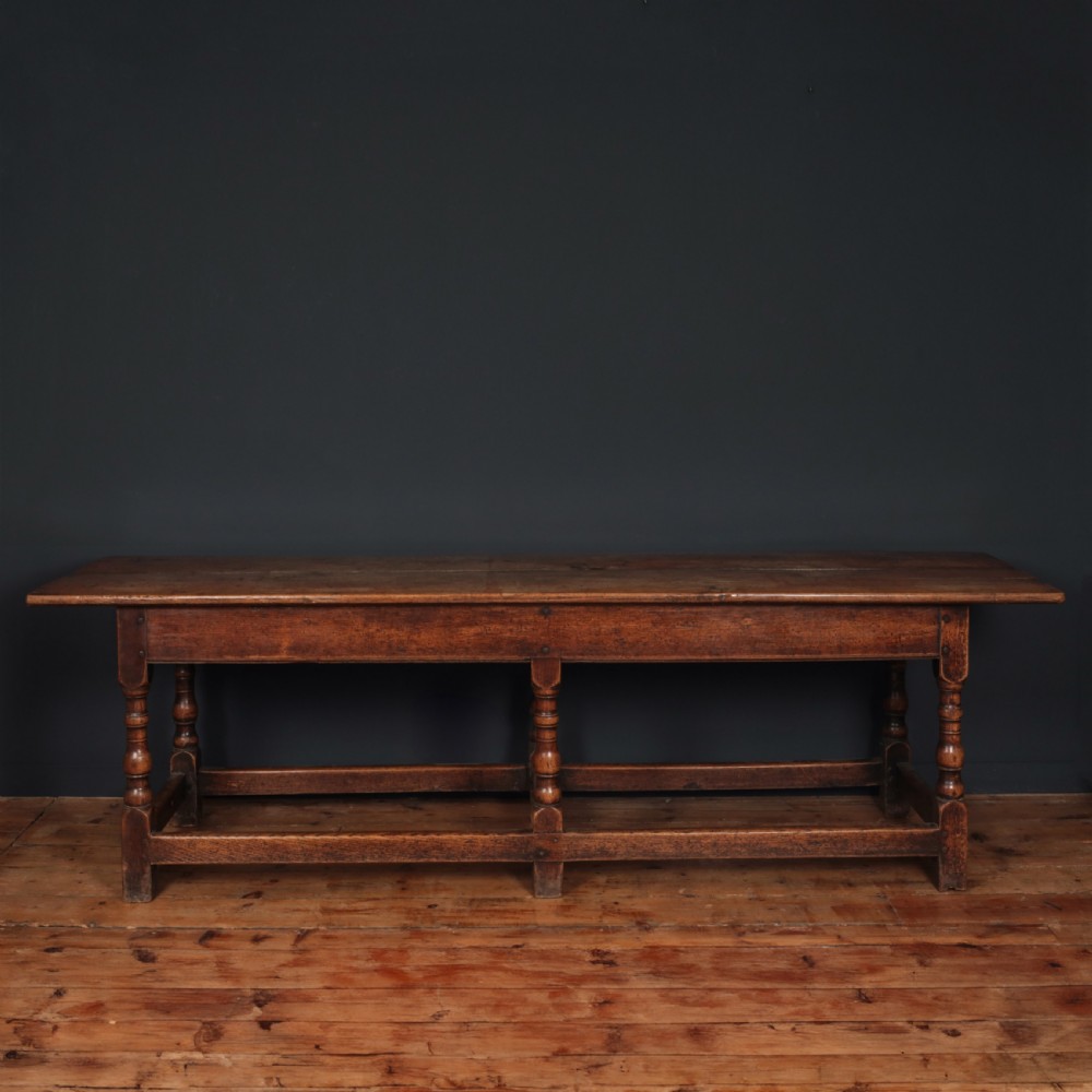 A long 17th-century oak refectory table featuring turned baluster legs, low stretchers, and a thick plank top.
