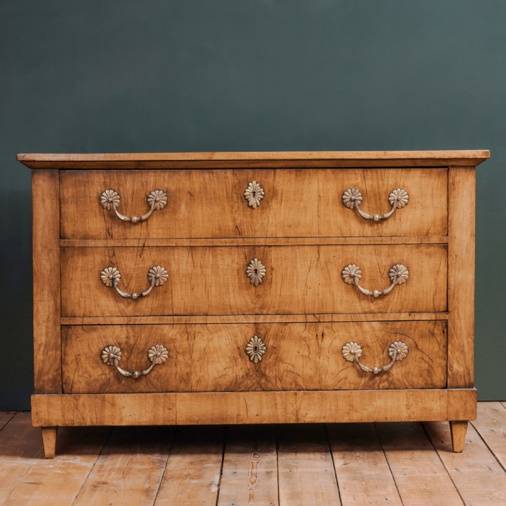 An 18th-century walnut commode featuring three wide drawers decorated with brass rosette swing handles and keyhole escutcheons on tapered feet.