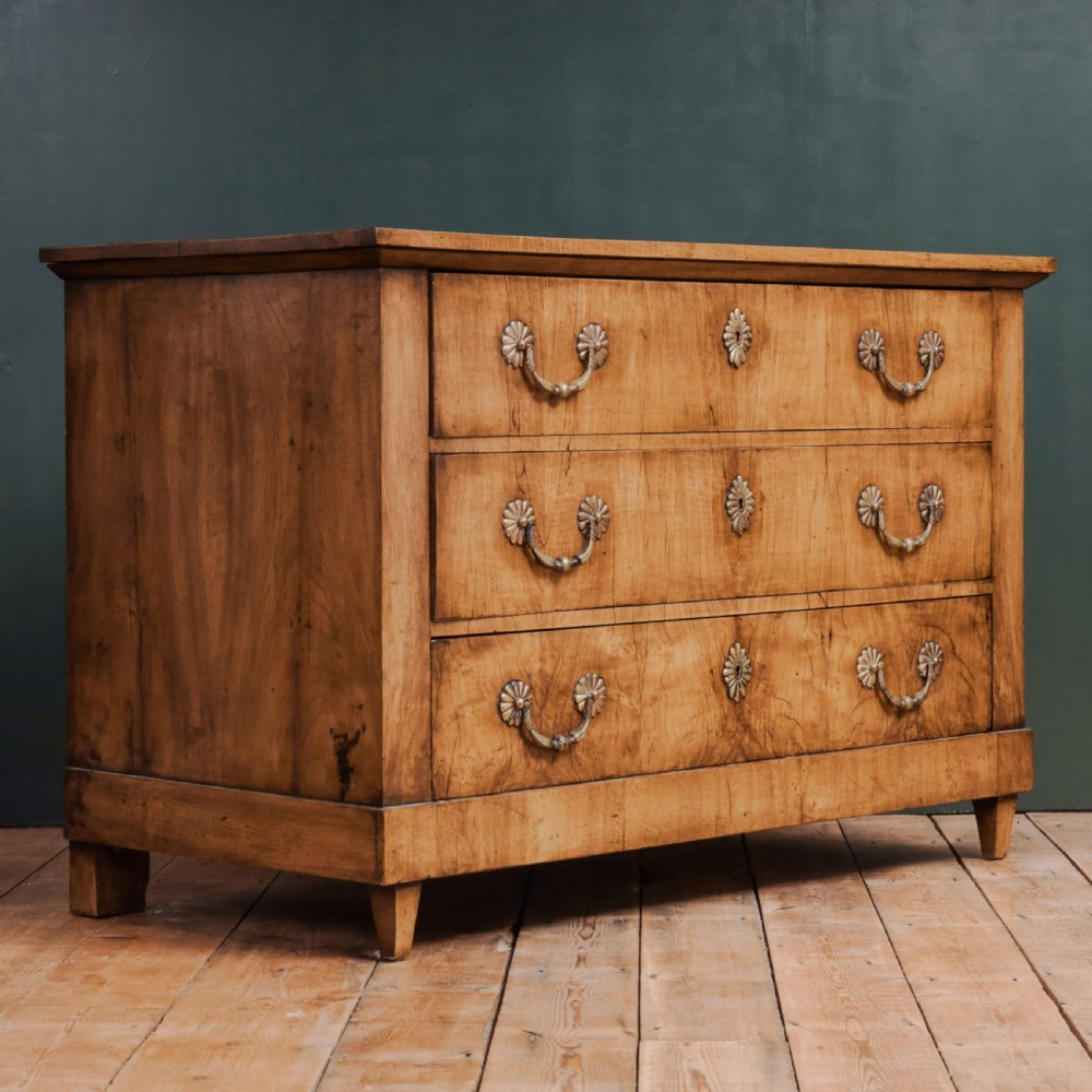 An 18th-century walnut commode featuring three wide drawers decorated with brass rosette swing handles and keyhole escutcheons on tapered feet. View VI