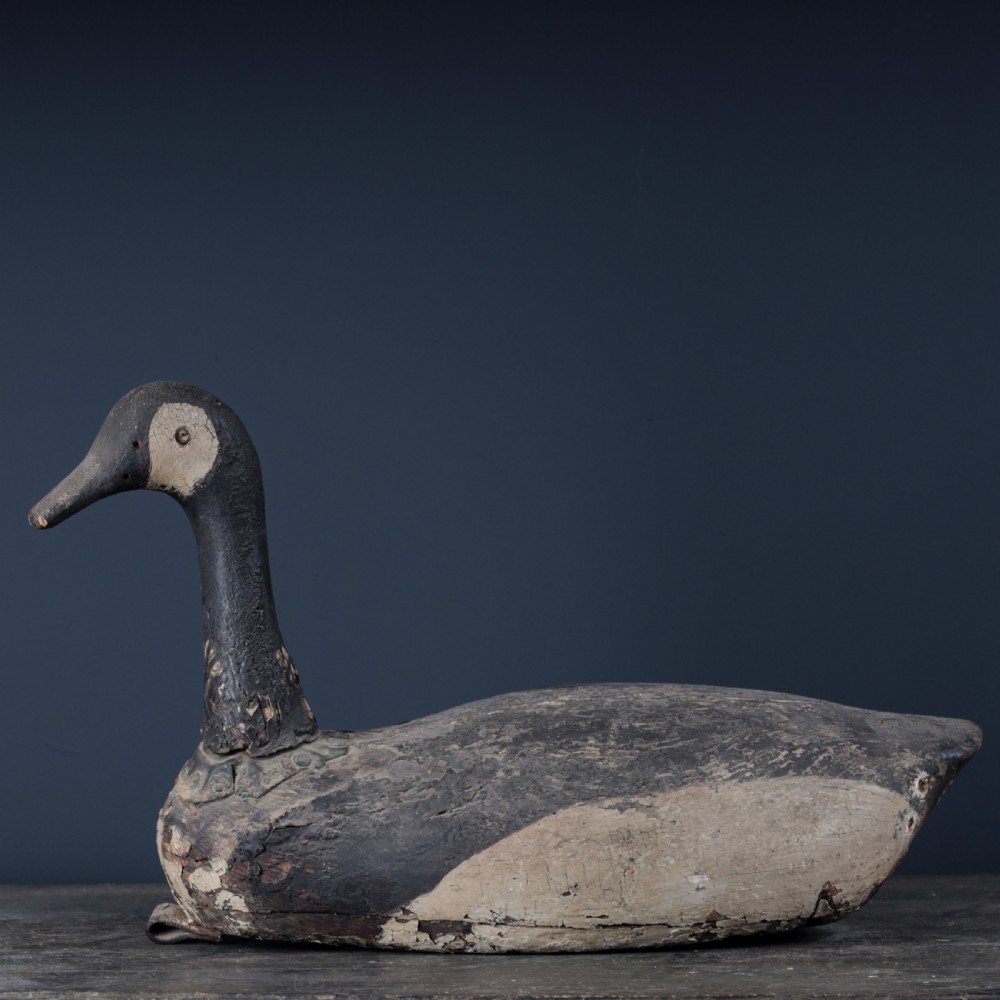 A 19th-century hand-carved wooden Canada goose decoy featuring distressed black and off-white paint with visible wear and natural patina.
