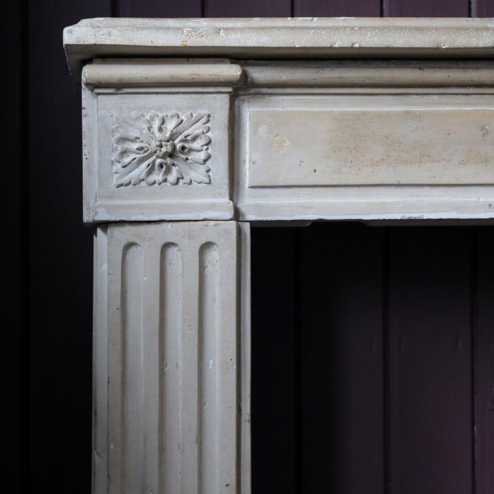 An off-white 18th-century stone fire surround featuring fluted pilasters, floral corner rosettes, and a moulded mantelshelf. View II