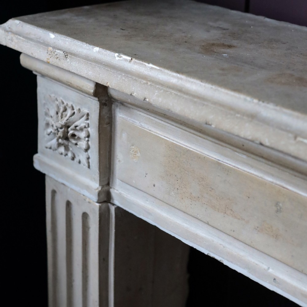 An off-white 18th-century stone fire surround featuring fluted pilasters, floral corner rosettes, and a moulded mantelshelf. View III