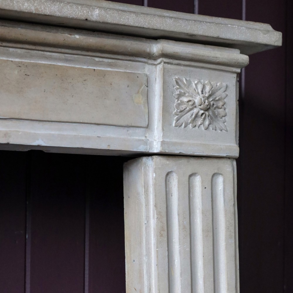 An off-white 18th-century stone fire surround featuring fluted pilasters, floral corner rosettes, and a moulded mantelshelf. View IV
