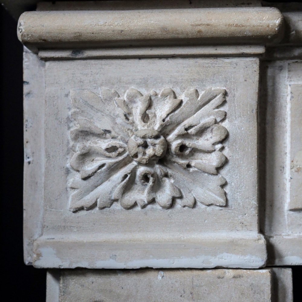 An off-white 18th-century stone fire surround featuring fluted pilasters, floral corner rosettes, and a moulded mantelshelf. View V