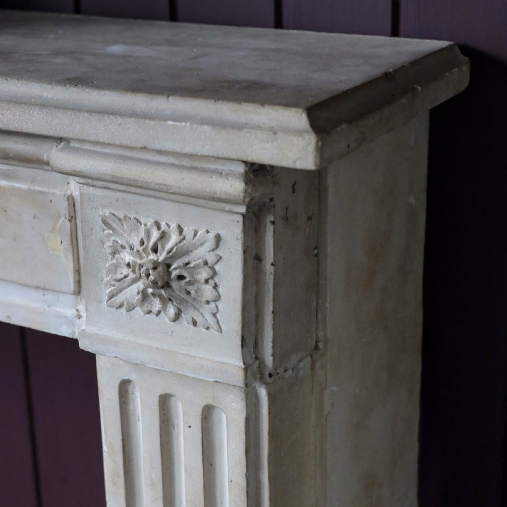 An off-white 18th-century stone fire surround featuring fluted pilasters, floral corner rosettes, and a moulded mantelshelf. View VII