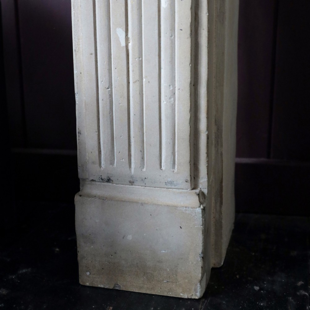 An off-white 18th-century stone fire surround featuring fluted pilasters, floral corner rosettes, and a moulded mantelshelf. View VIII
