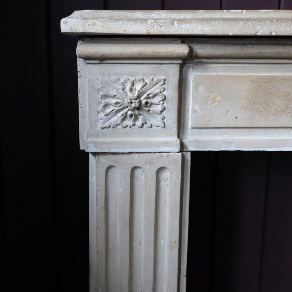 An off-white 18th-century stone fire surround featuring fluted pilasters, floral corner rosettes, and a moulded mantelshelf. View XII