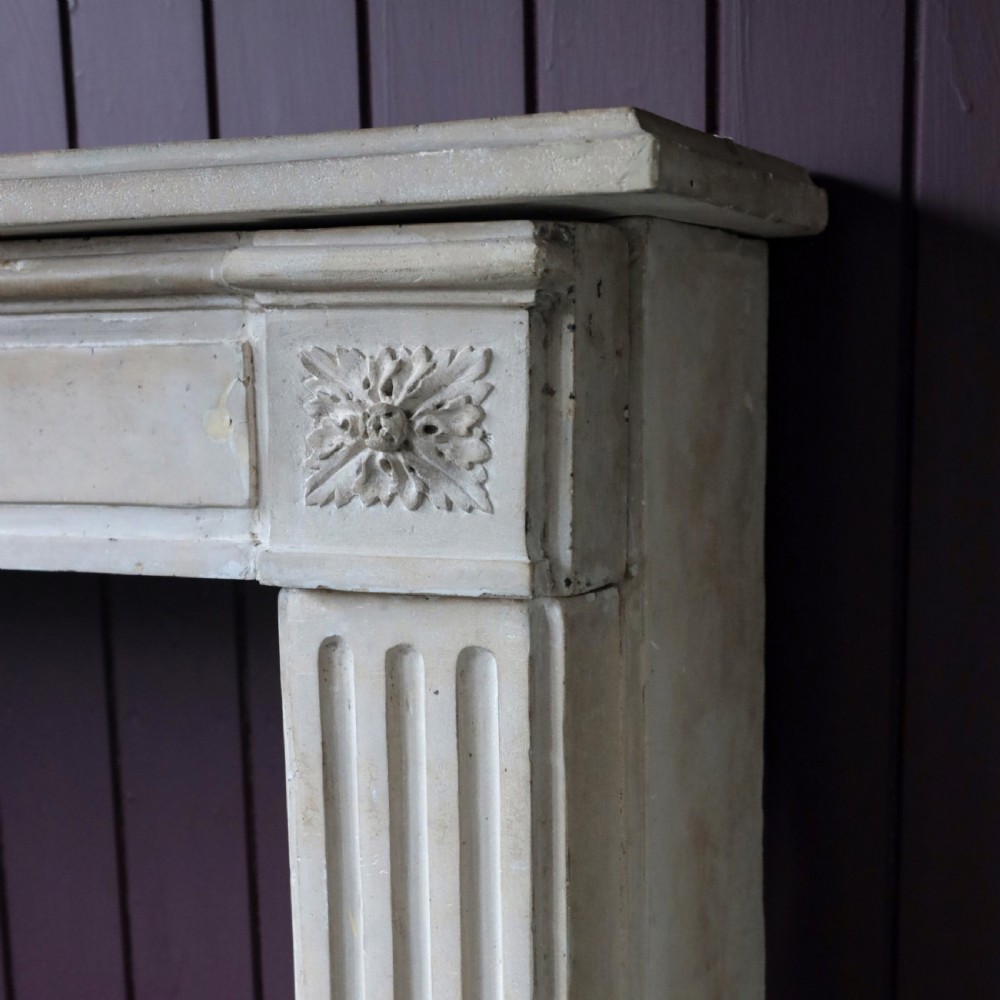 An off-white 18th-century stone fire surround featuring fluted pilasters, floral corner rosettes, and a moulded mantelshelf. View XIII
