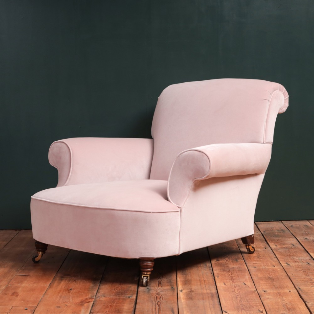 A 19th-century low-slung armchair upholstered in pale pink velvet, featuring rolled arms, a scrolled back, and turned front legs on brass castors.