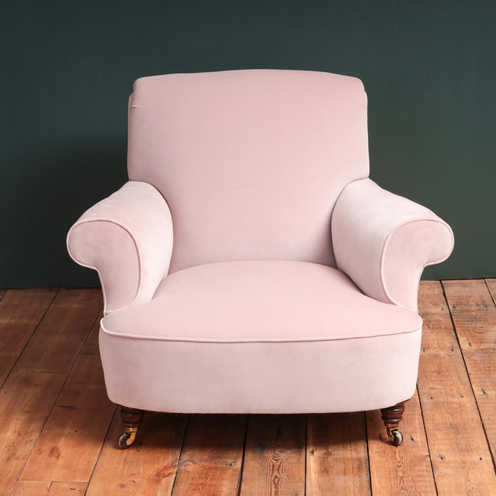 A 19th-century low-slung armchair upholstered in pale pink velvet, featuring rolled arms, a scrolled back, and turned front legs on brass castors. View IV