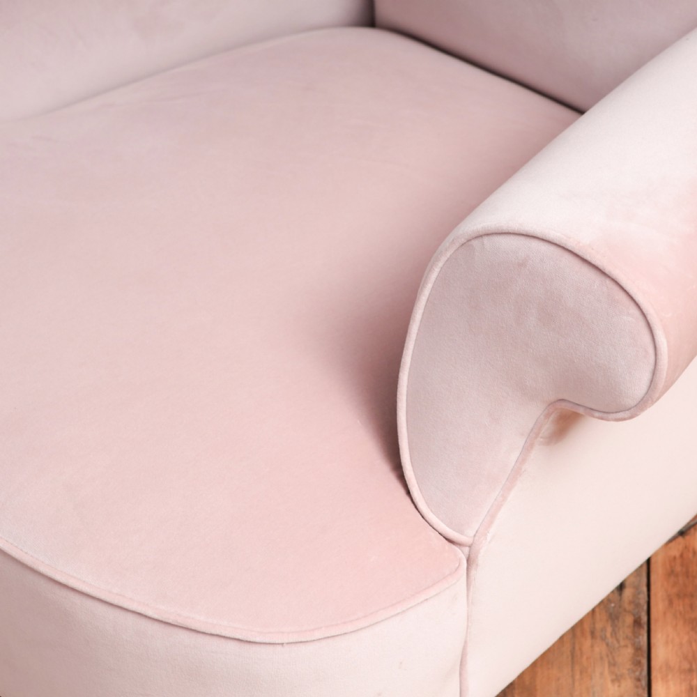 A 19th-century low-slung armchair upholstered in pale pink velvet, featuring rolled arms, a scrolled back, and turned front legs on brass castors. View VI