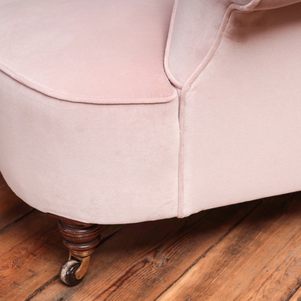 A 19th-century low-slung armchair upholstered in pale pink velvet, featuring rolled arms, a scrolled back, and turned front legs on brass castors. View VIII