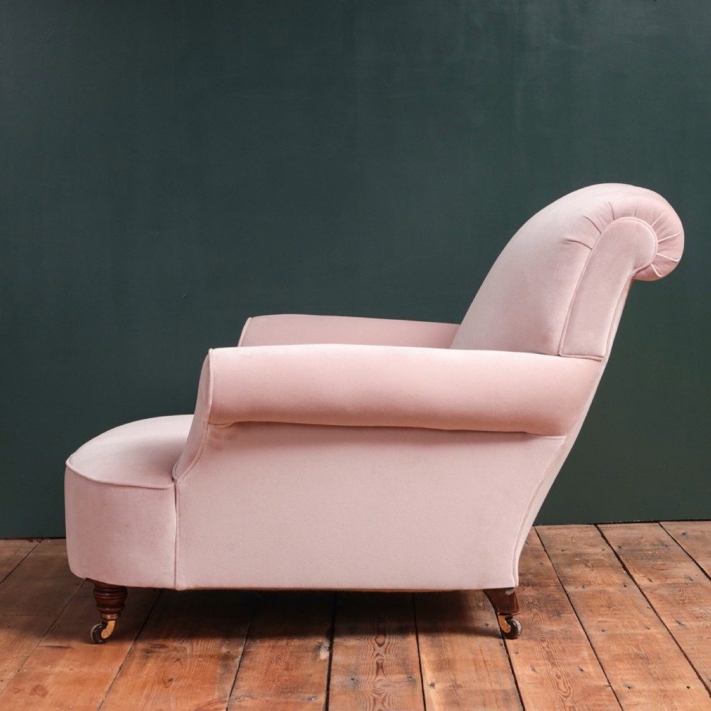 A 19th-century low-slung armchair upholstered in pale pink velvet, featuring rolled arms, a scrolled back, and turned front legs on brass castors. View IX