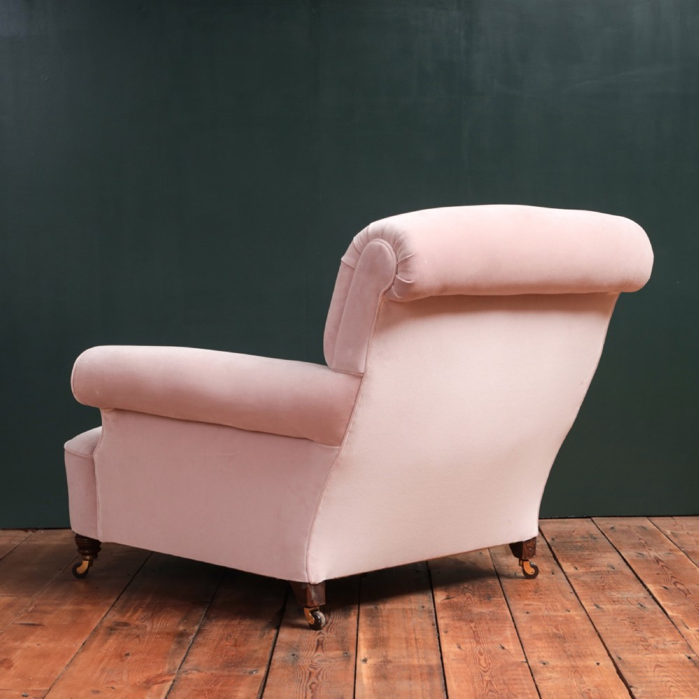 A 19th-century low-slung armchair upholstered in pale pink velvet, featuring rolled arms, a scrolled back, and turned front legs on brass castors. View XI