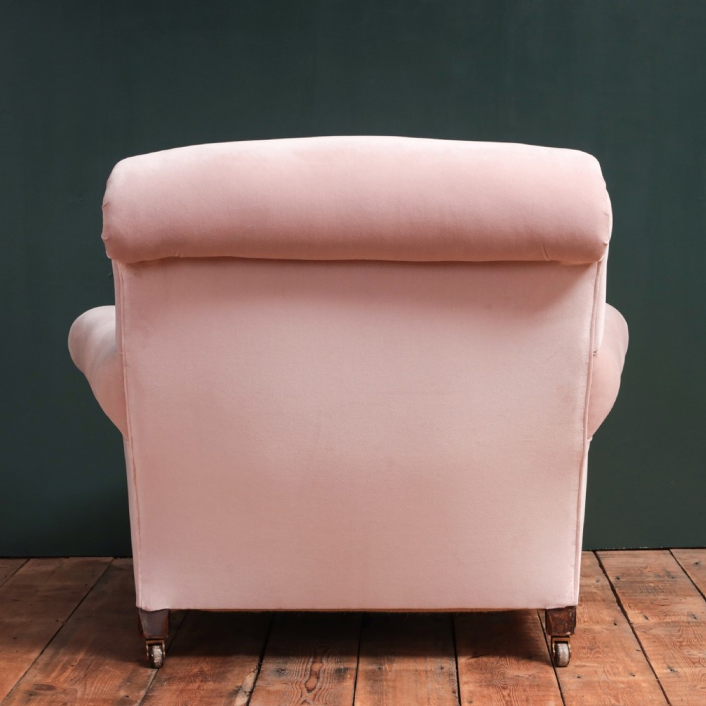 A 19th-century low-slung armchair upholstered in pale pink velvet, featuring rolled arms, a scrolled back, and turned front legs on brass castors. View XII