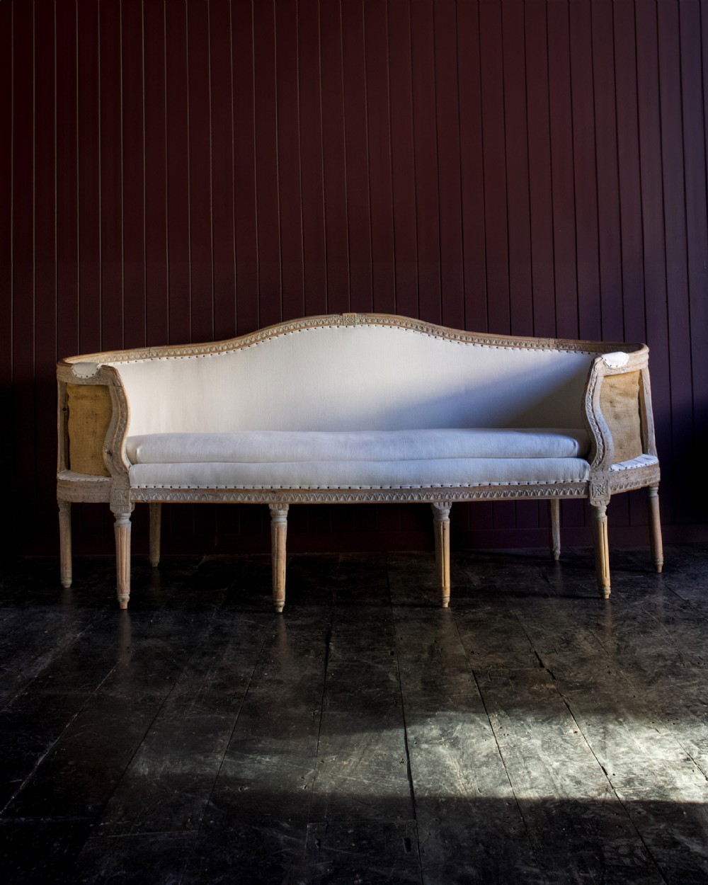An 18th-century Swedish Gustavian sofa featuring a carved wooden frame with fluted legs, light linen upholstery, and exposed hessian side construction.