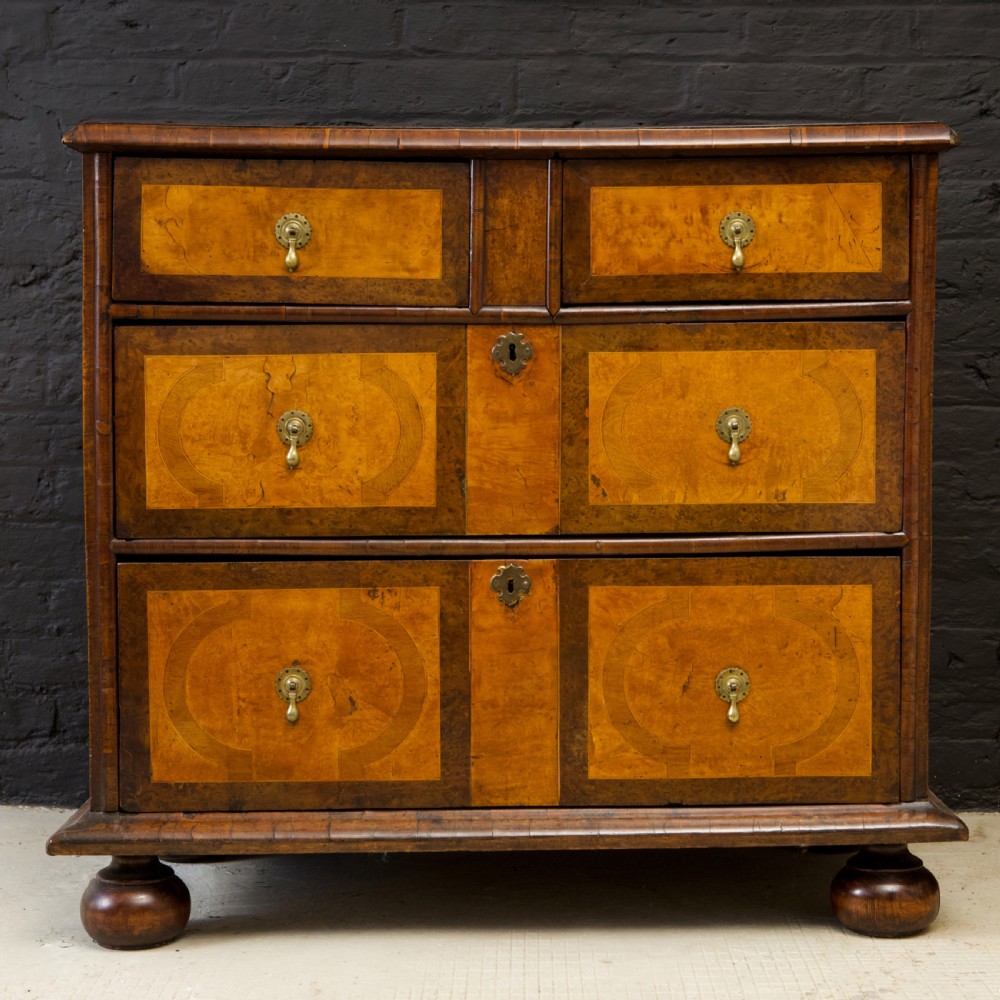 A late 17th-century William and Mary chest of drawers crafted from yew and maple featuring geometric inlaid panels, teardrop brass handles, and turned bun feet.