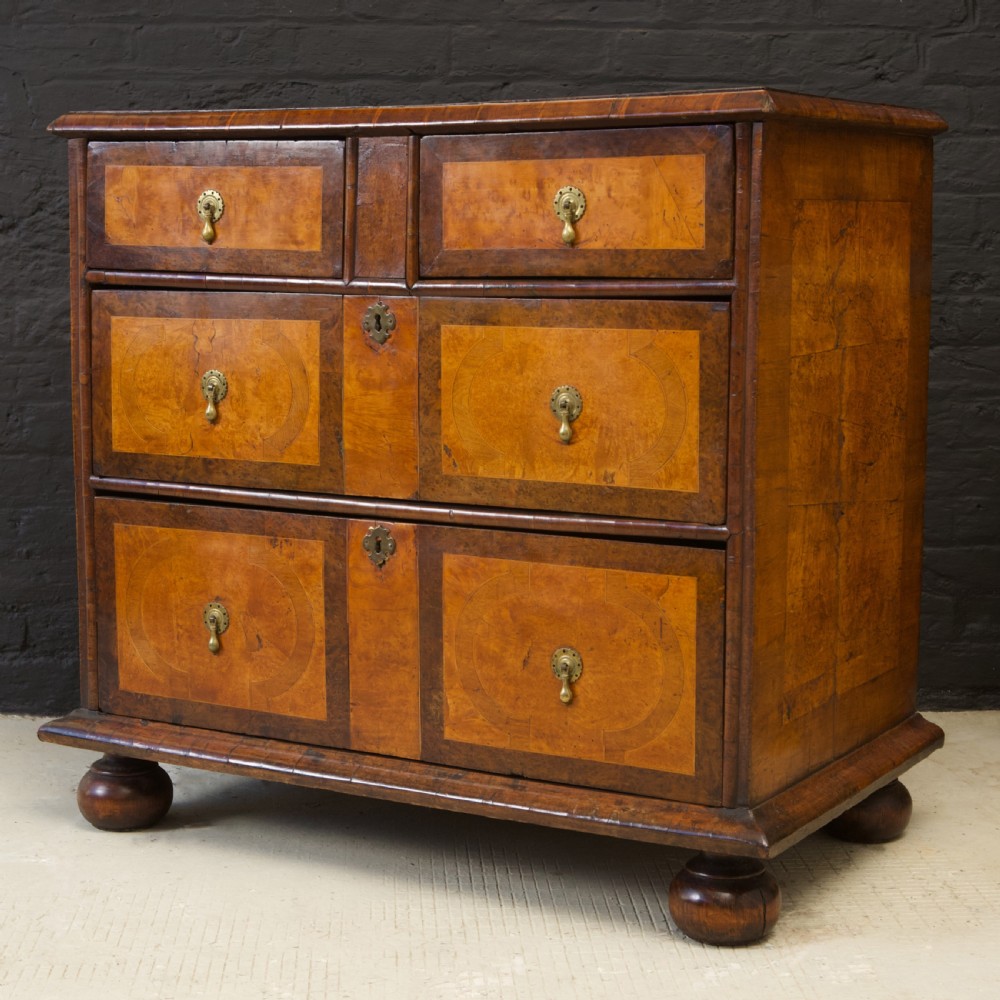 A late 17th-century William and Mary chest of drawers crafted from yew and maple featuring geometric inlaid panels, teardrop brass handles, and turned bun feet. View V